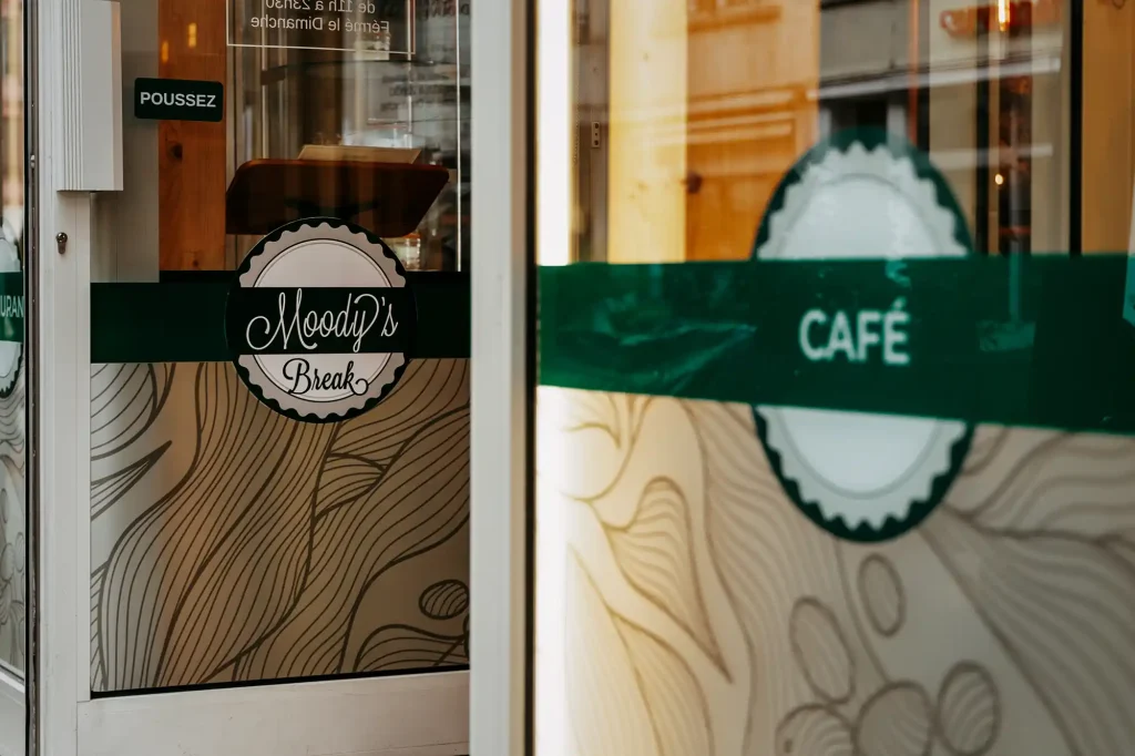 Installation de vitrophanie décorative sur la vitrine du restaurant Moody's Break, alliant esthétisme et visibilité en plein centre-ville.